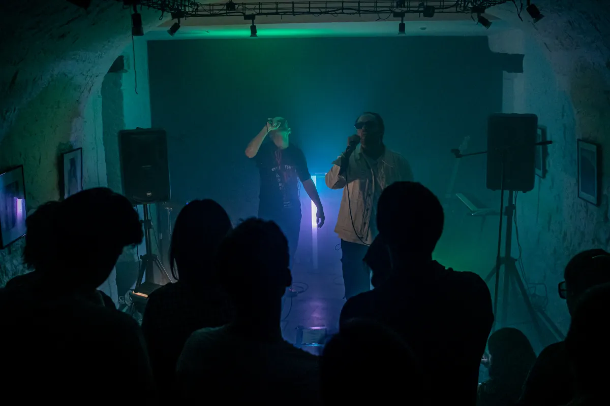 MAAD AVENUE on stage in a vaulted cellar, two band members in green and blue light and fog, the audience in silhouette